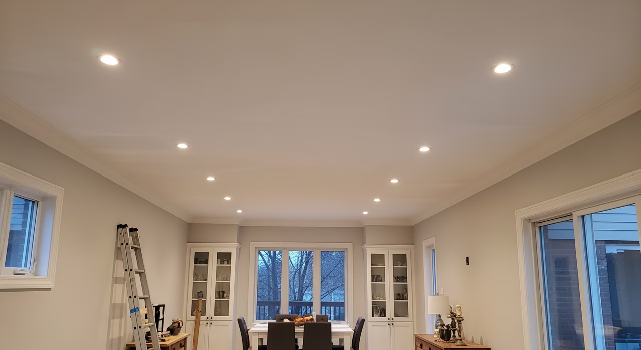 Completed Toronto great-room with newly-installed 5/8-inch Type C 1-hr fire-rated drywall ceiling over wood joists per OBC 9.10.9.16, taped Level 4 finish primed and painted Benjamin Moore Chantilly Lace matte ceiling-white, freshly-removed popcorn texture skim-coated smooth, recessed LED pot lights